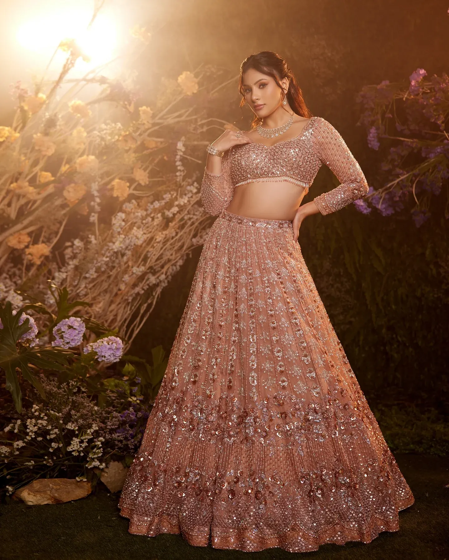 A blush lehenga with dense bead work, photographed among pale blooms.