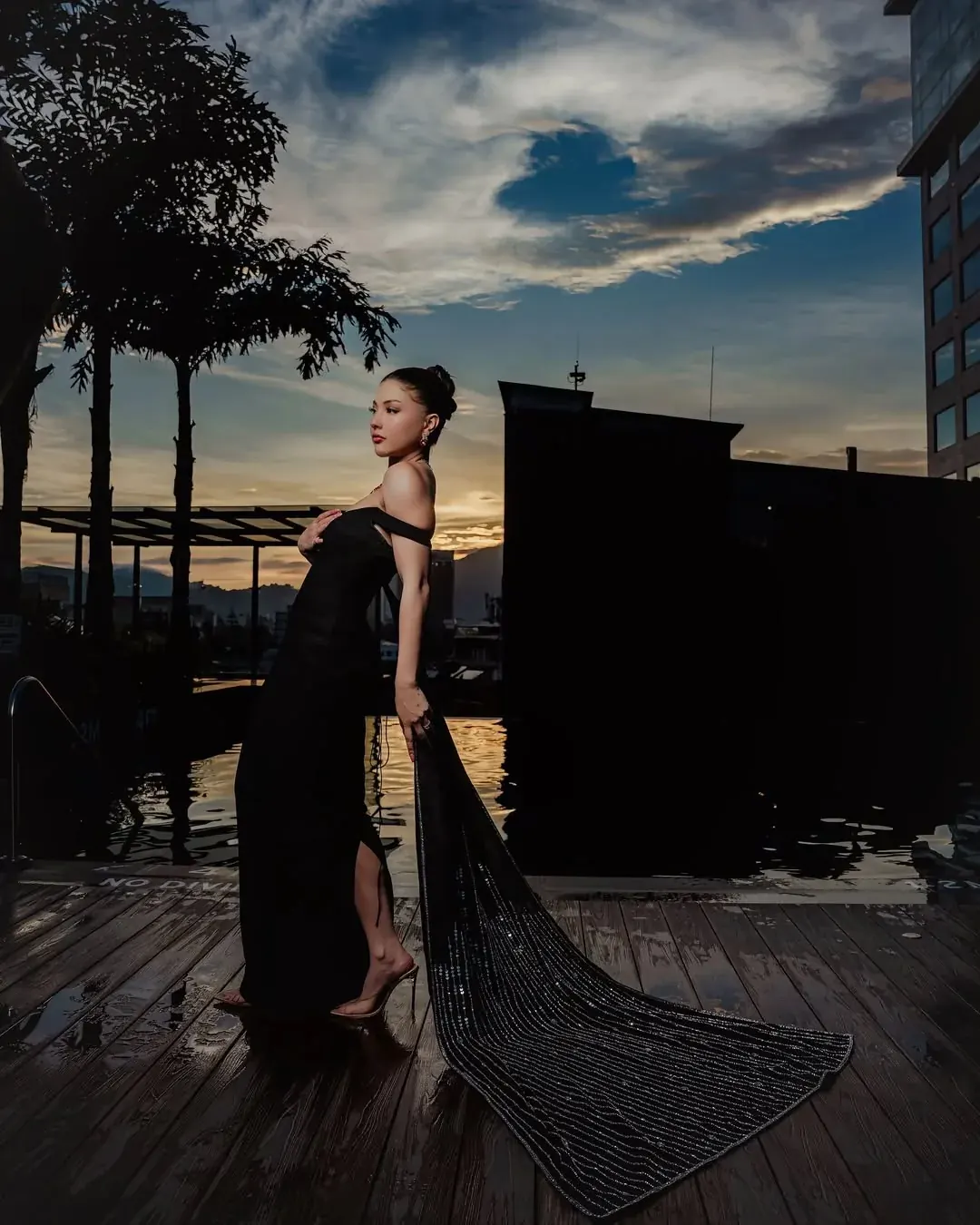 A black gown with a long beaded train, photographed on a deck at dusk.