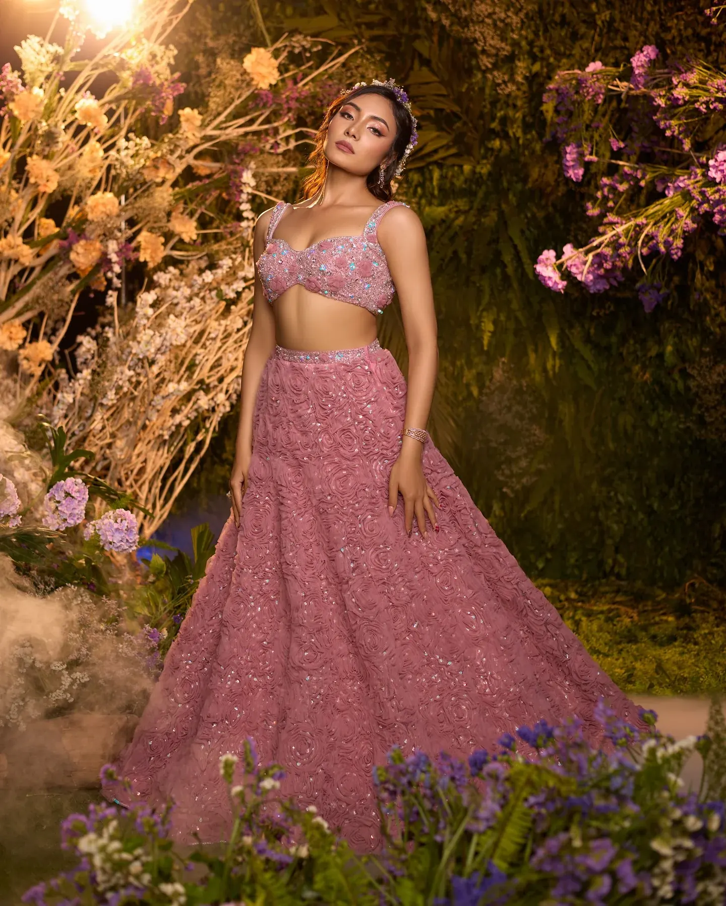 A pink lehenga with scattered bead work, photographed among flowers and foliage.