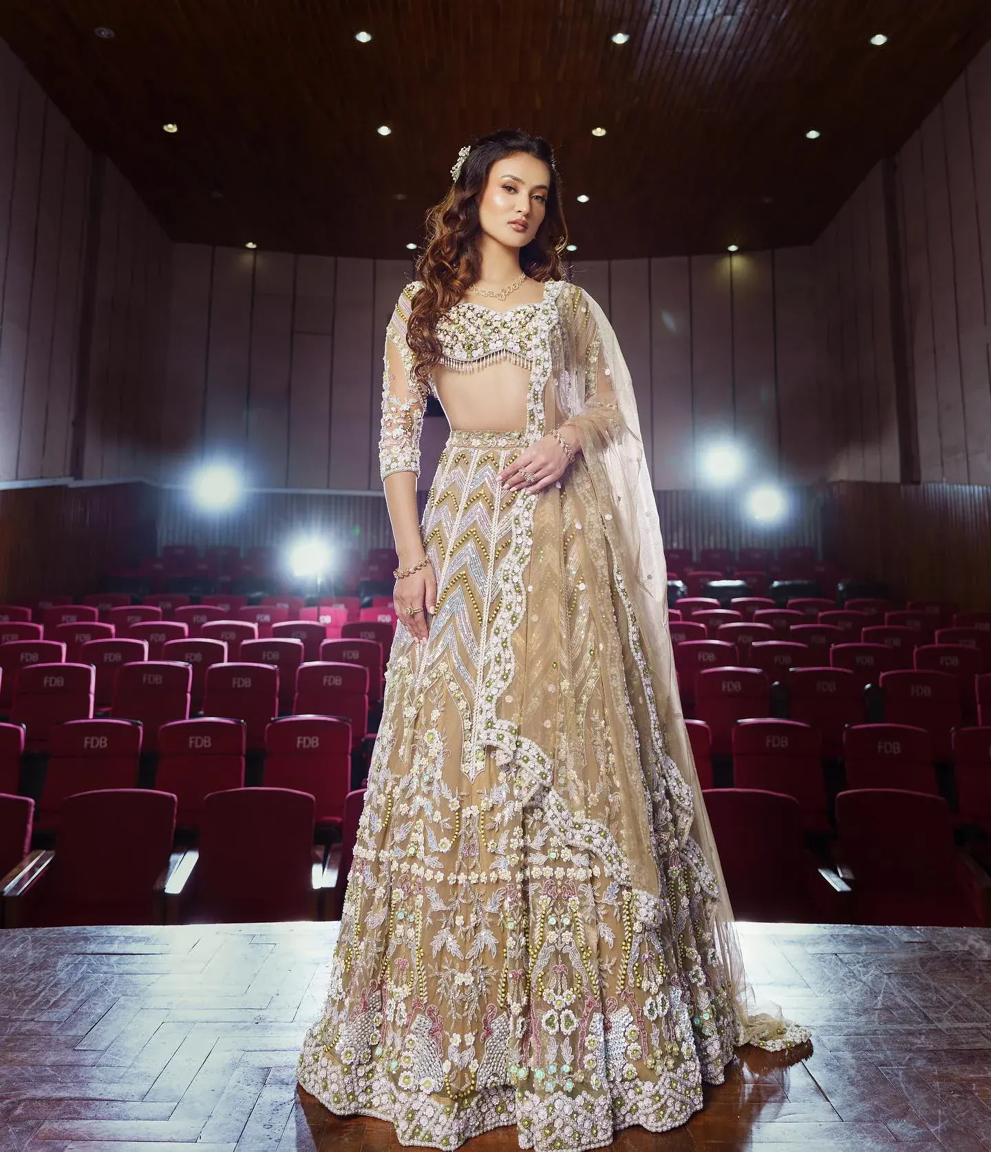 A champagne lehenga with gold embroidery and a sheer dupatta, photographed on a lit stage.