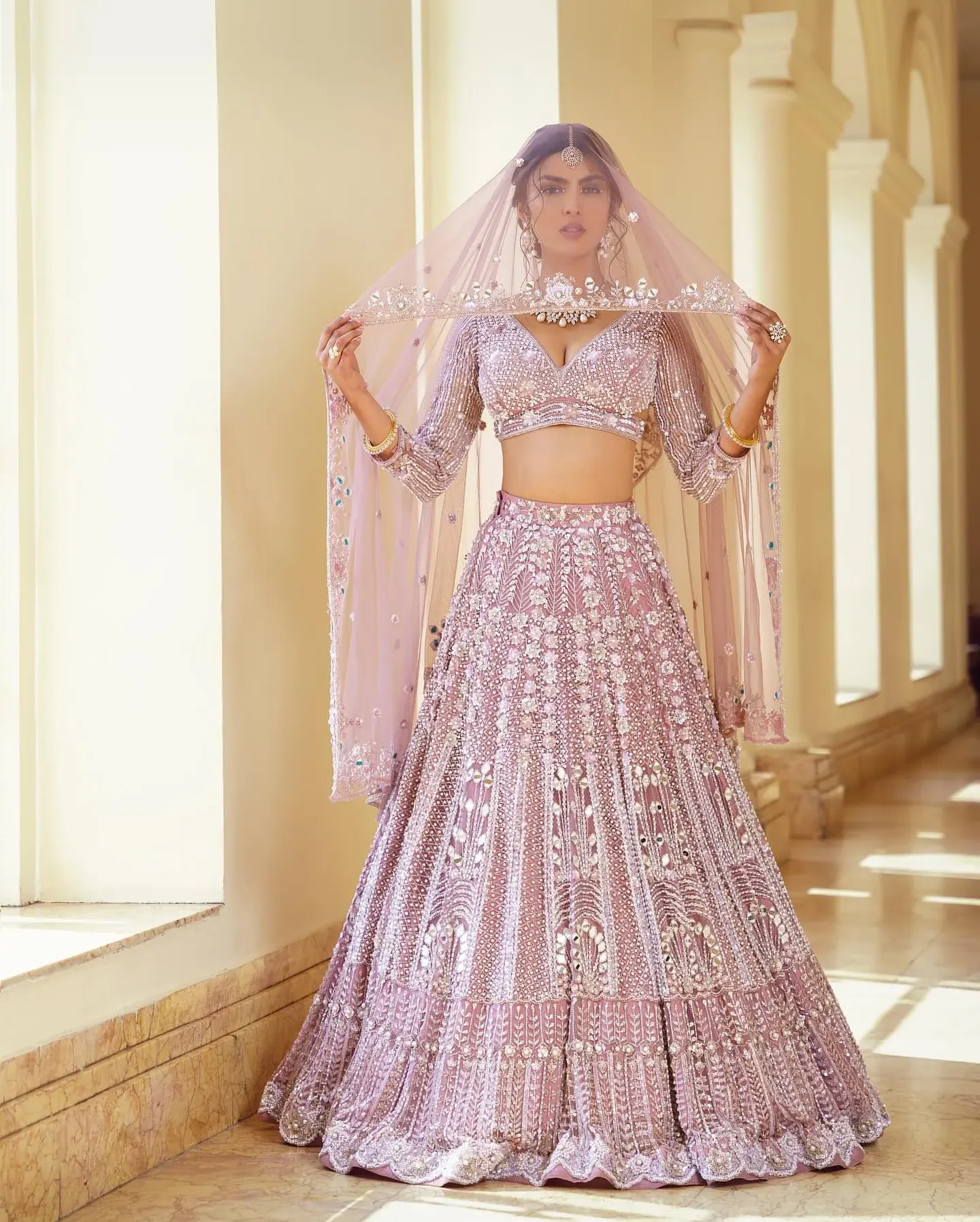 A lilac lehenga with scalloped embroidery and a sheer veil, beside a colonnade.