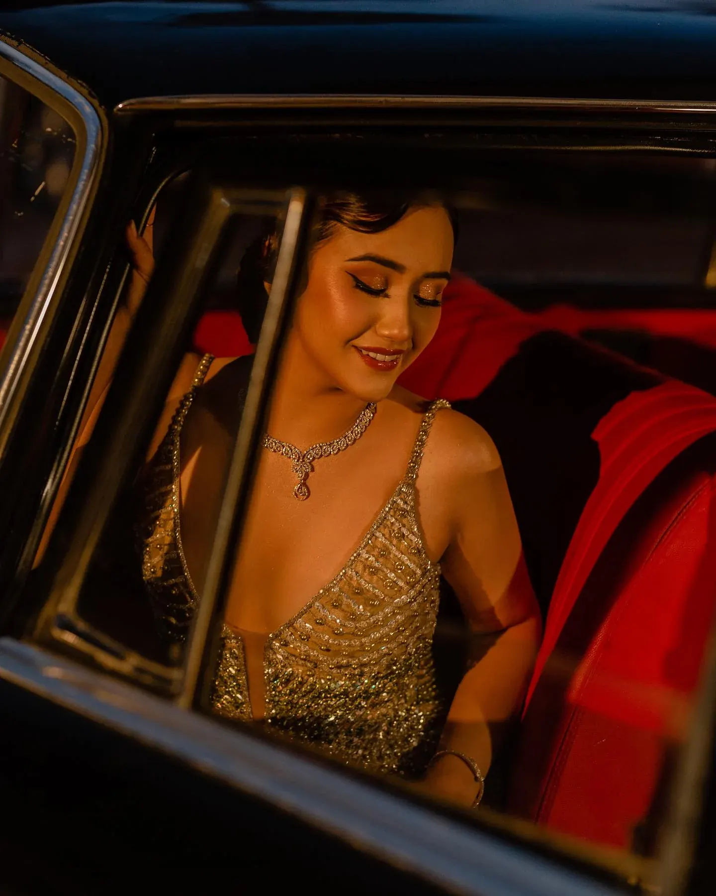 A gold beaded gown photographed through the open door of a vintage car at night.