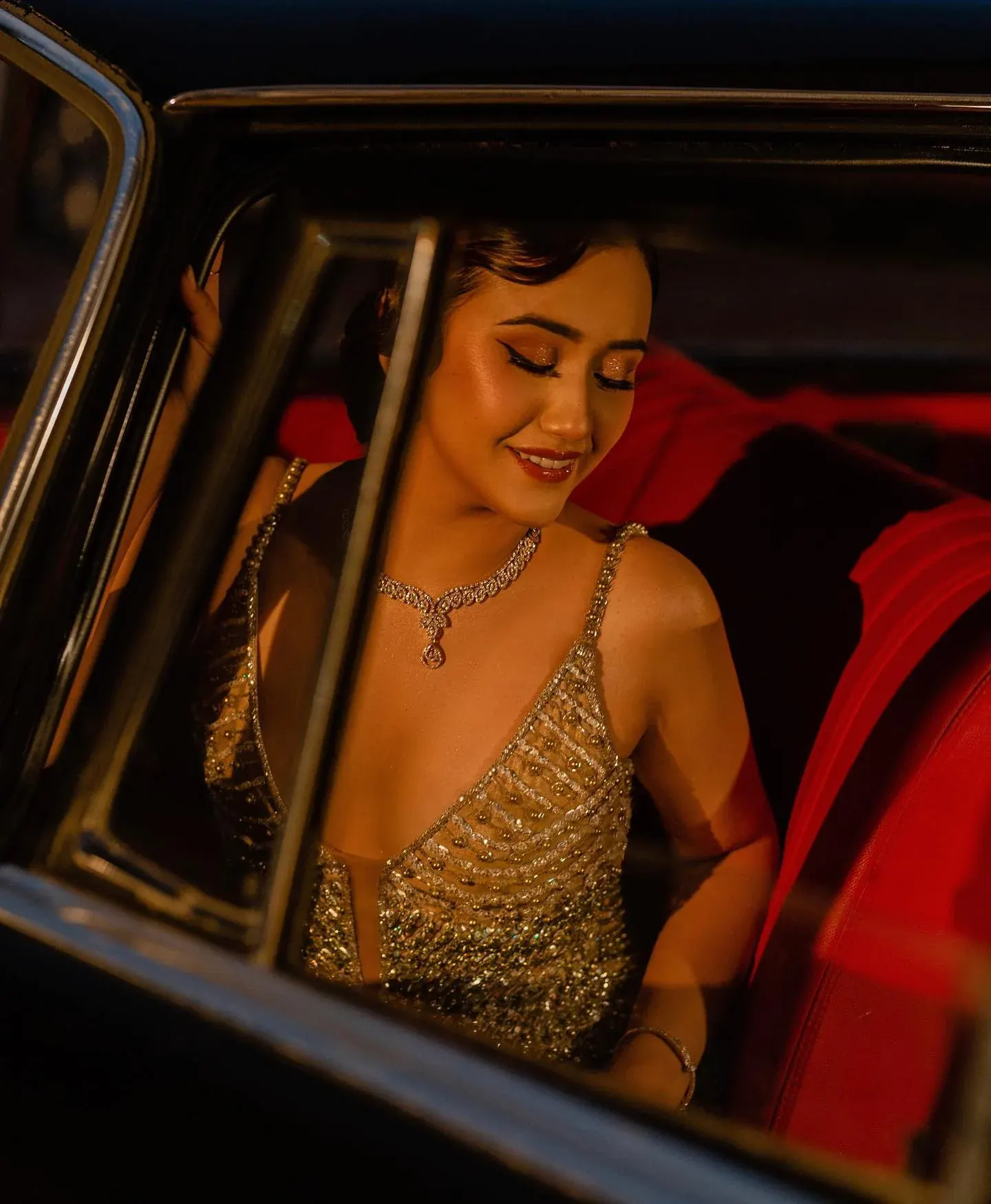 A gold beaded gown photographed through the window of a vintage car at night.