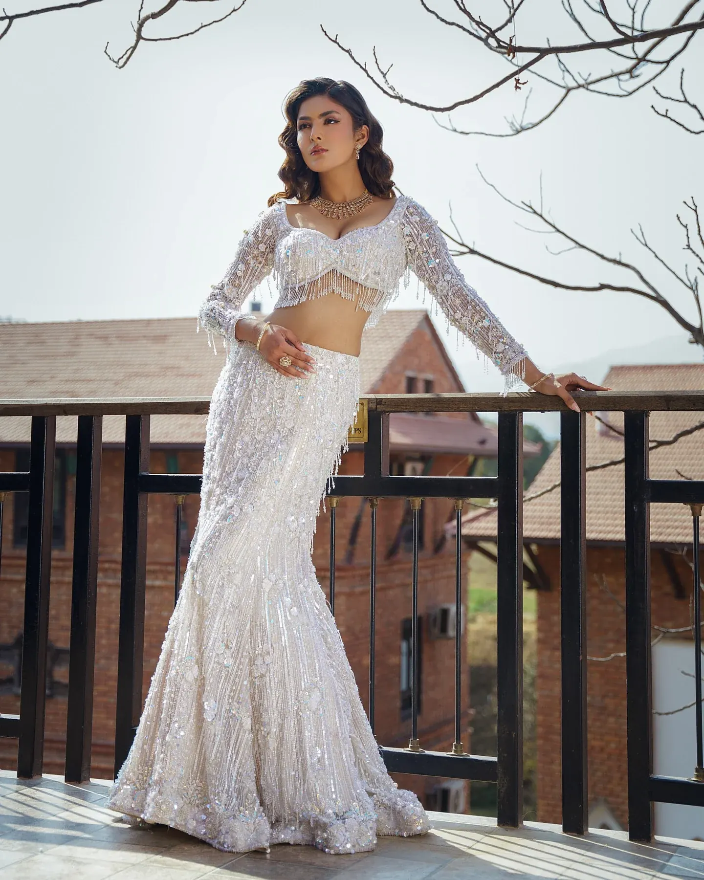 An ivory fishtail gown with sequinned embroidery and a maroon drape, on a terrace.