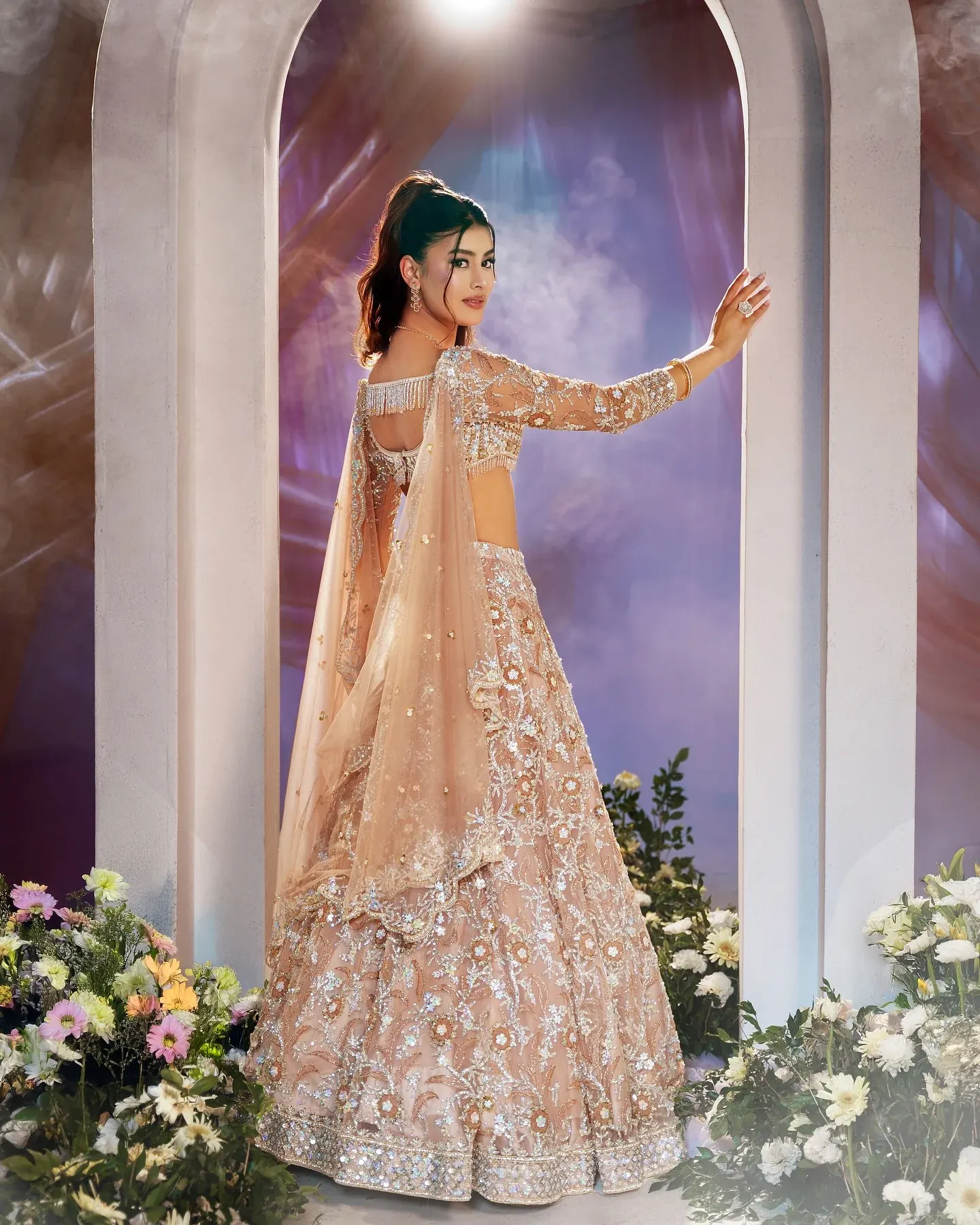 A champagne lehenga with floral embroidery, photographed beneath a pale arch.