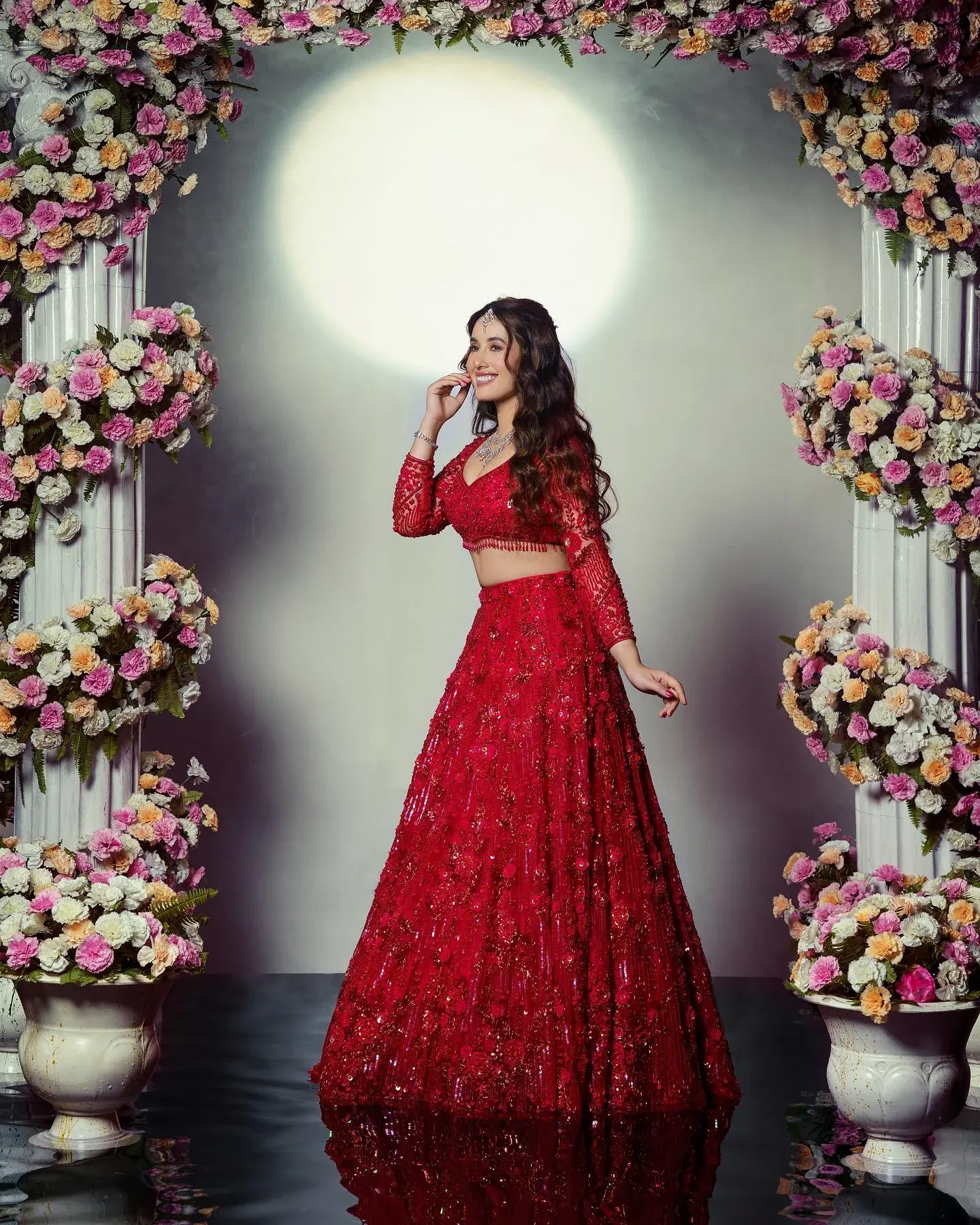 A red lehenga with dense embroidery, photographed beneath an arch of flowers.