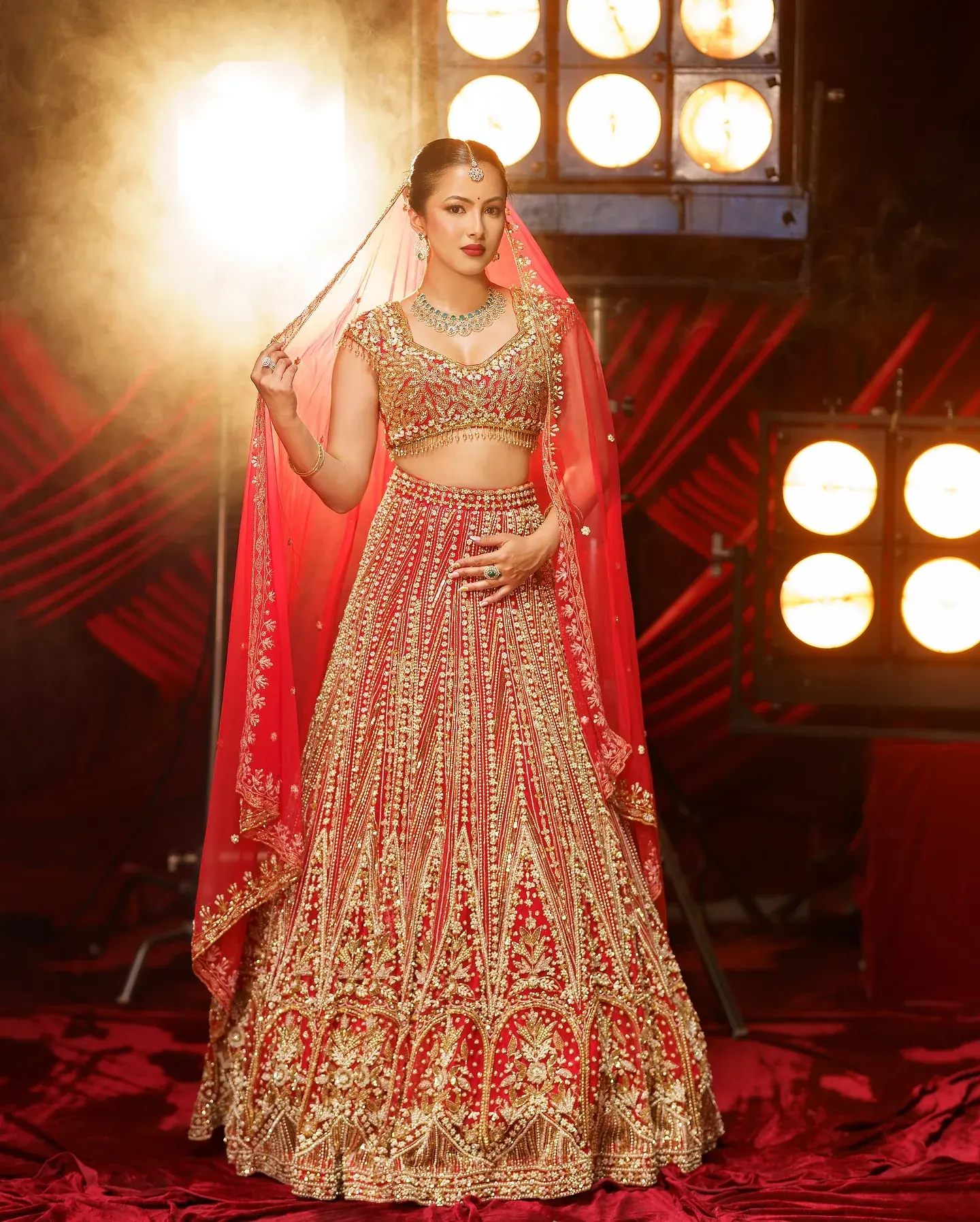A gold lehenga with dense embroidery and a red veil, photographed under studio lights.