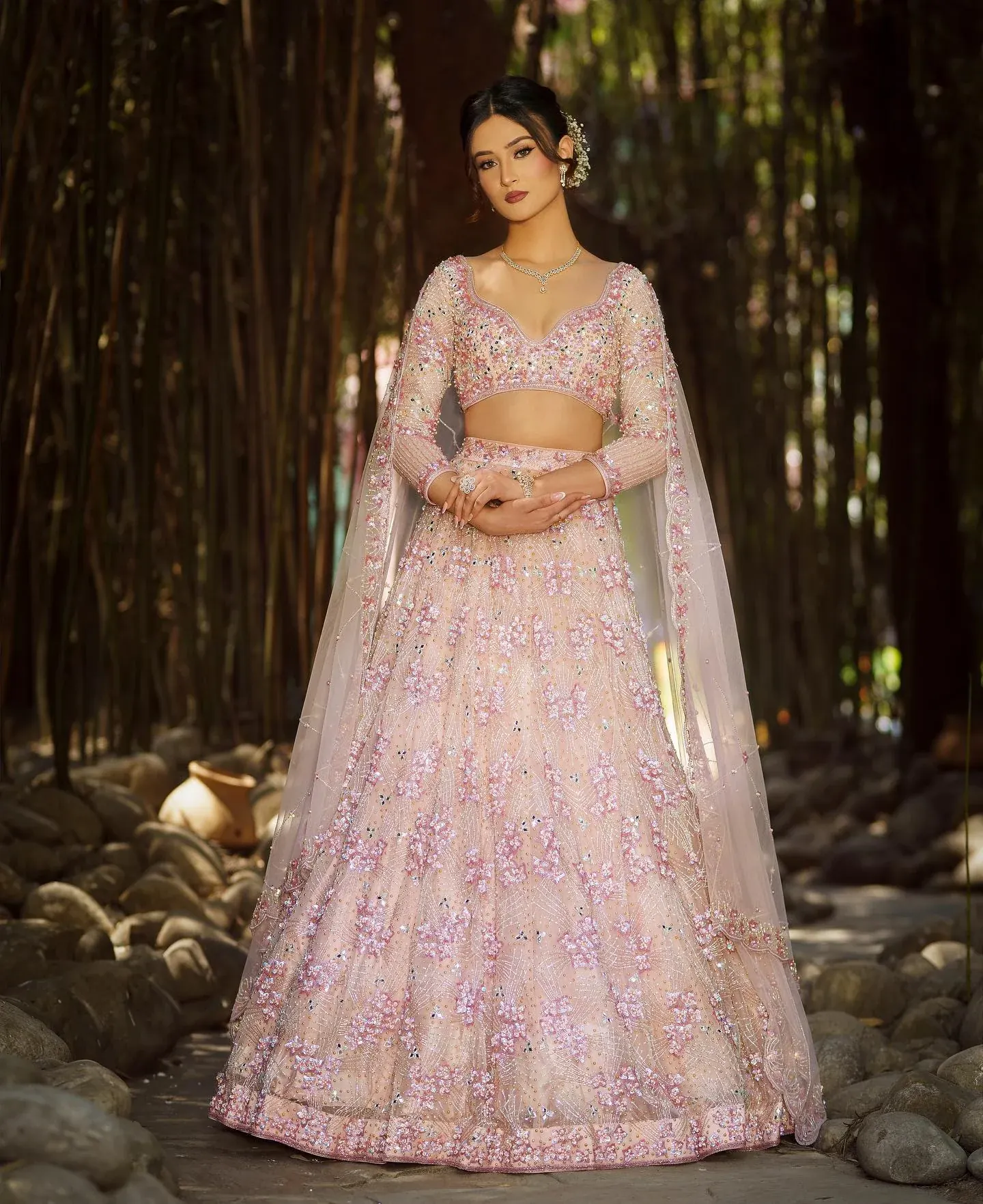 A blush lehenga with a sheer embroidered dupatta, photographed in a bamboo grove.