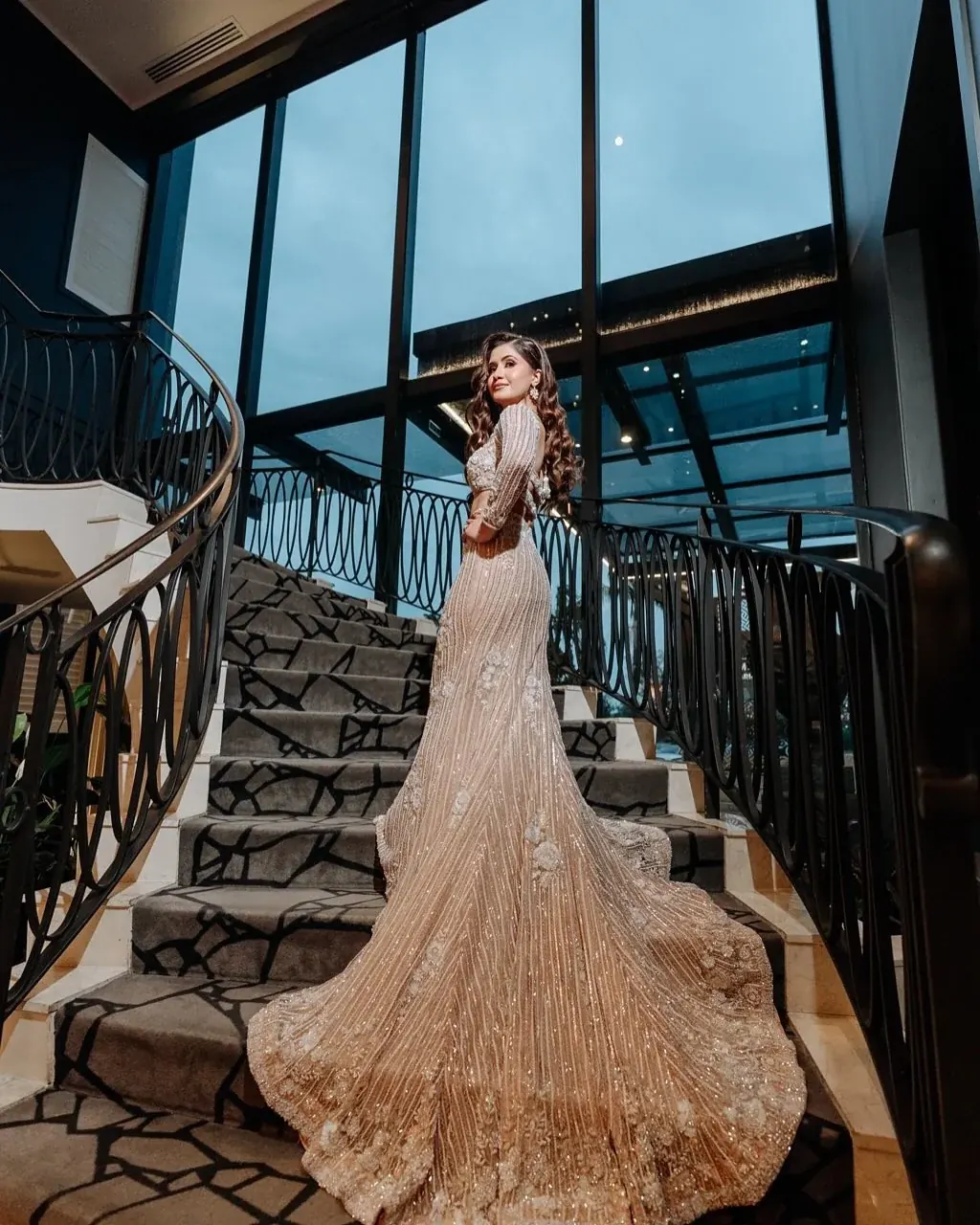 A champagne fishtail gown with a sequinned train, photographed on a curved staircase.