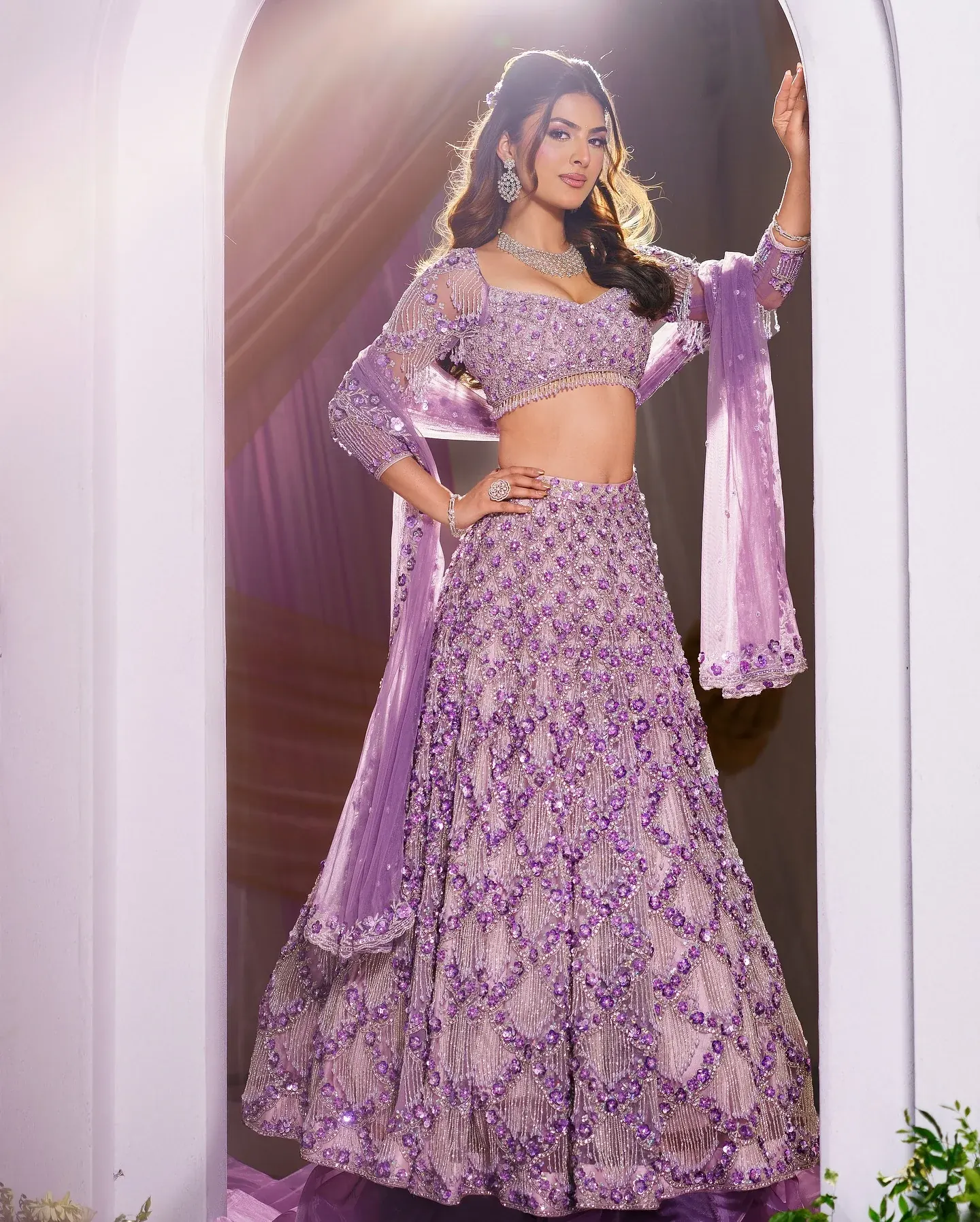 A lilac lehenga with dense bead work and a sheer dupatta, beneath a pale arch.