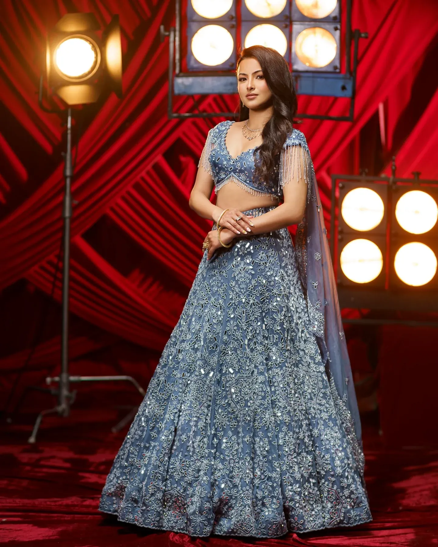 A pale blue lehenga with silver embroidery and a sheer dupatta, against red drapery.