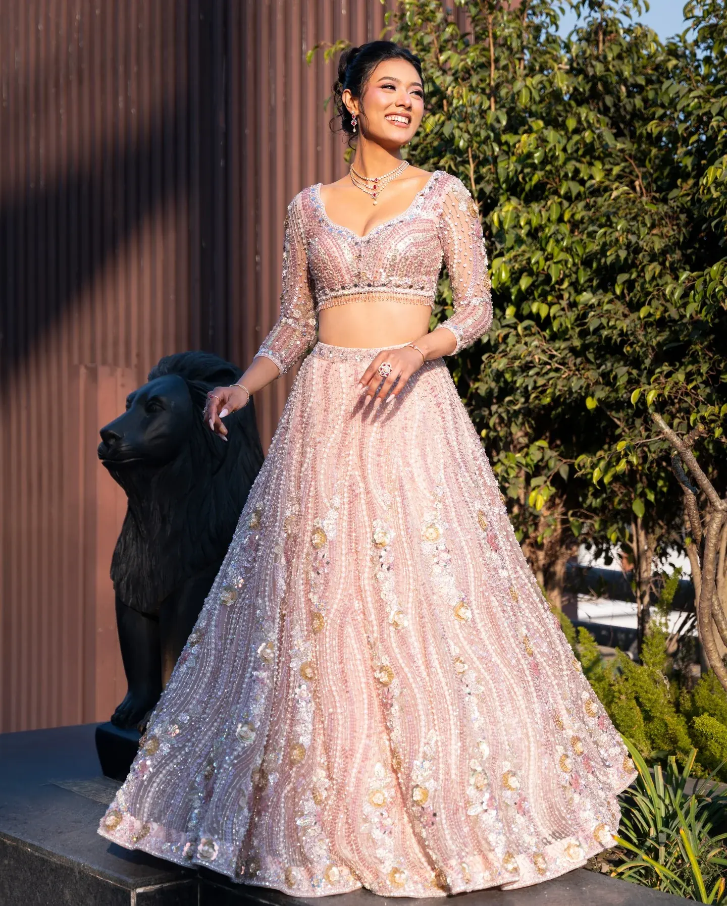 A blush lehenga with raised floral work and a sheer dupatta, photographed in a garden.