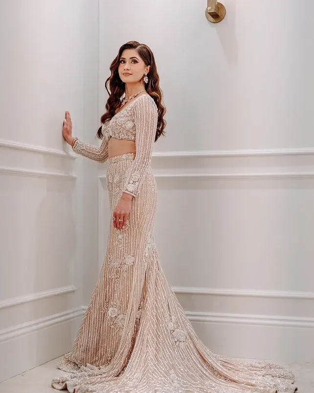 An ivory beaded gown with a long embroidered train, photographed against a panelled white wall.