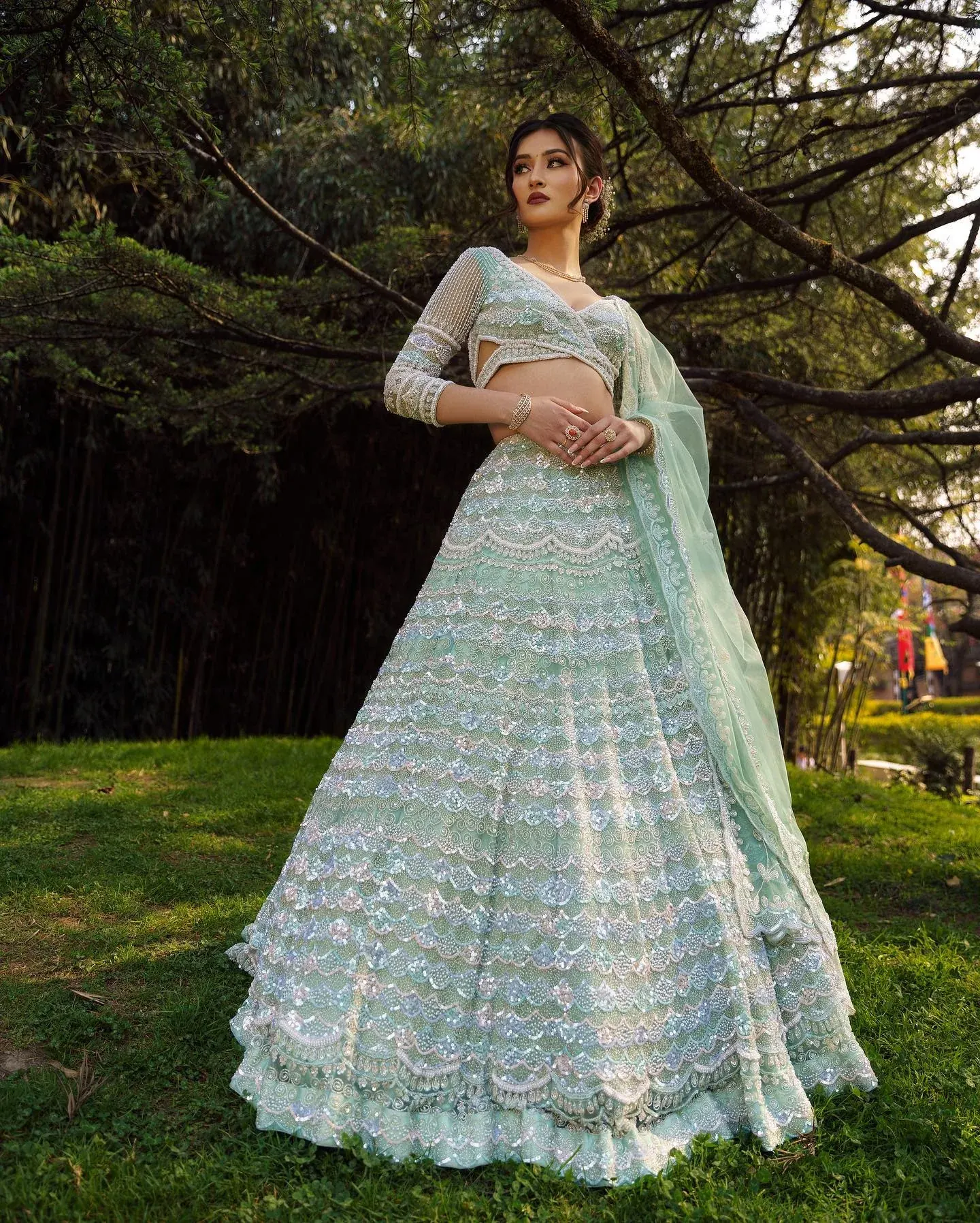 An aqua lehenga with tiered embroidery and a sheer dupatta, photographed on a lawn.