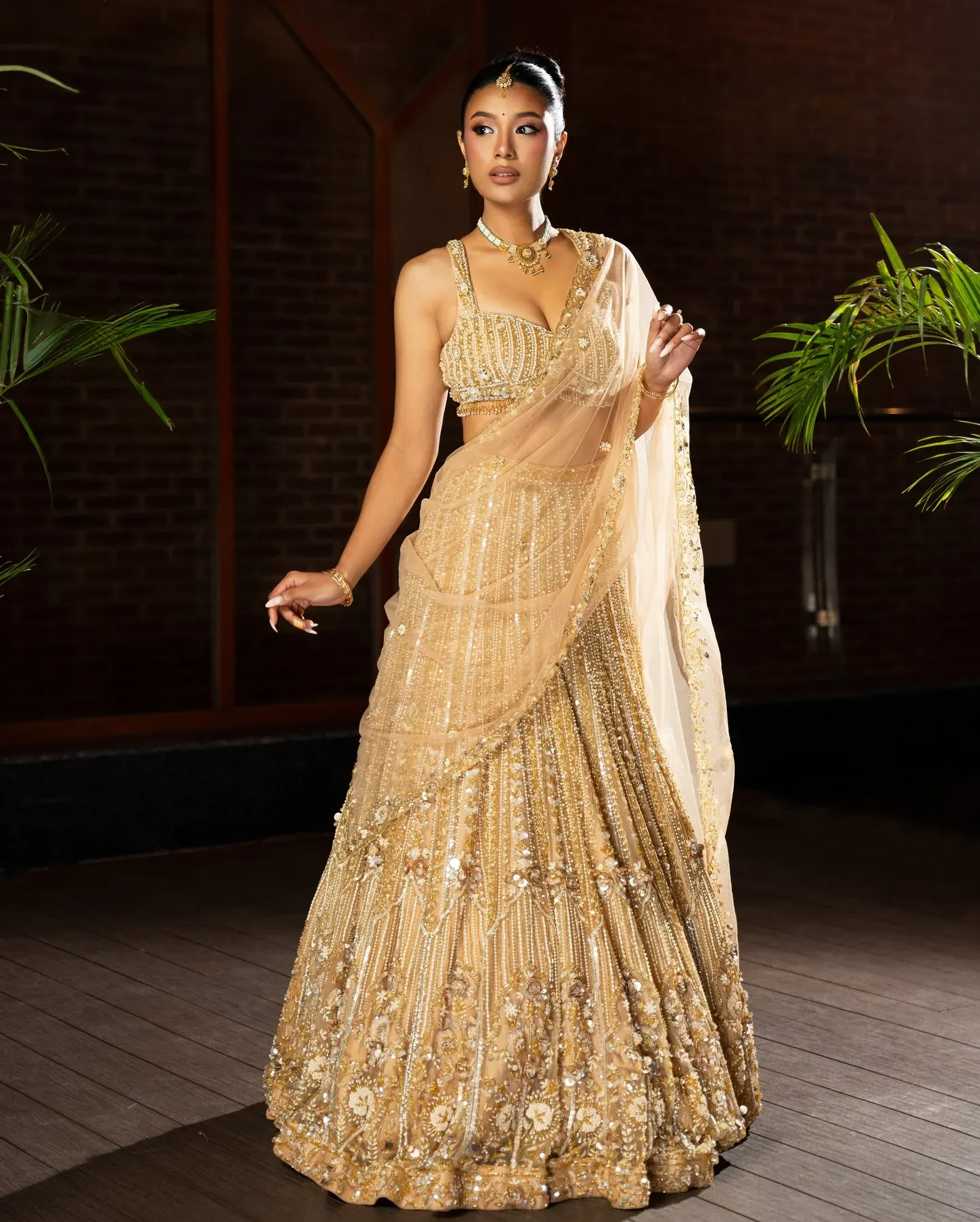 A gold saree in embroidered net with a beaded blouse, draped in a lamplit interior.