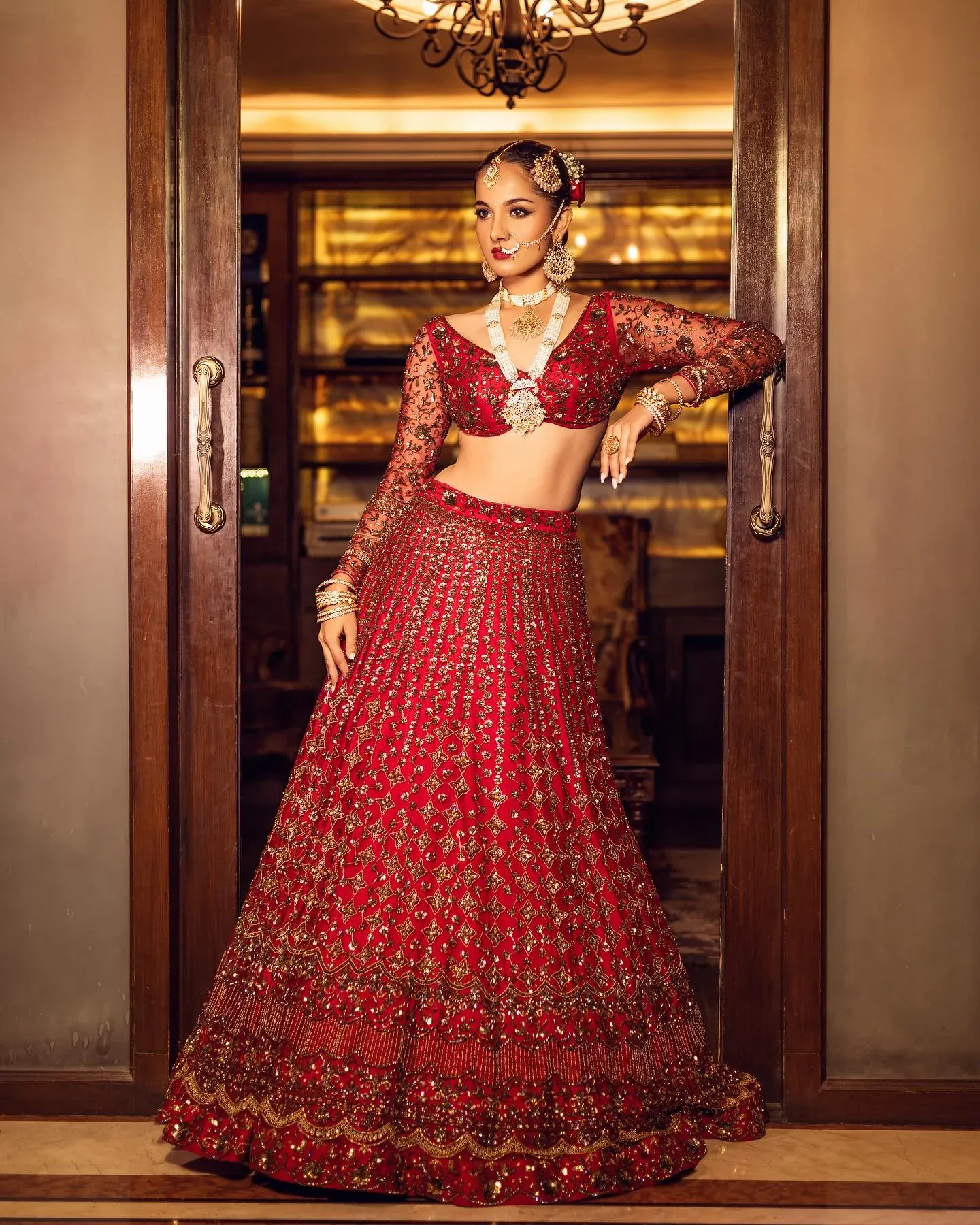 A red bridal lehenga with gold embroidery, photographed in a carved doorway.