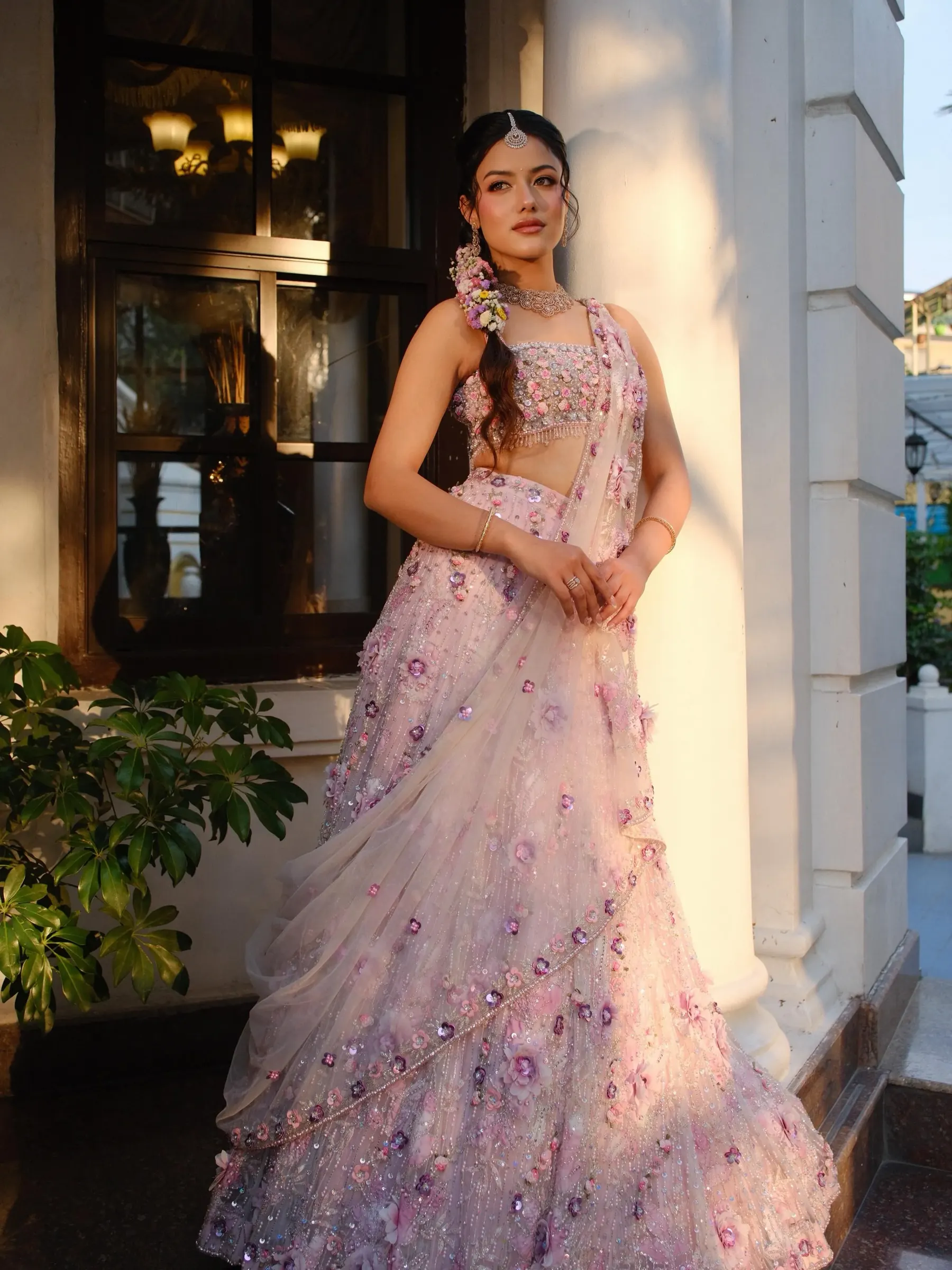 A blush lehenga with raised floral work, photographed against a lit facade at night.