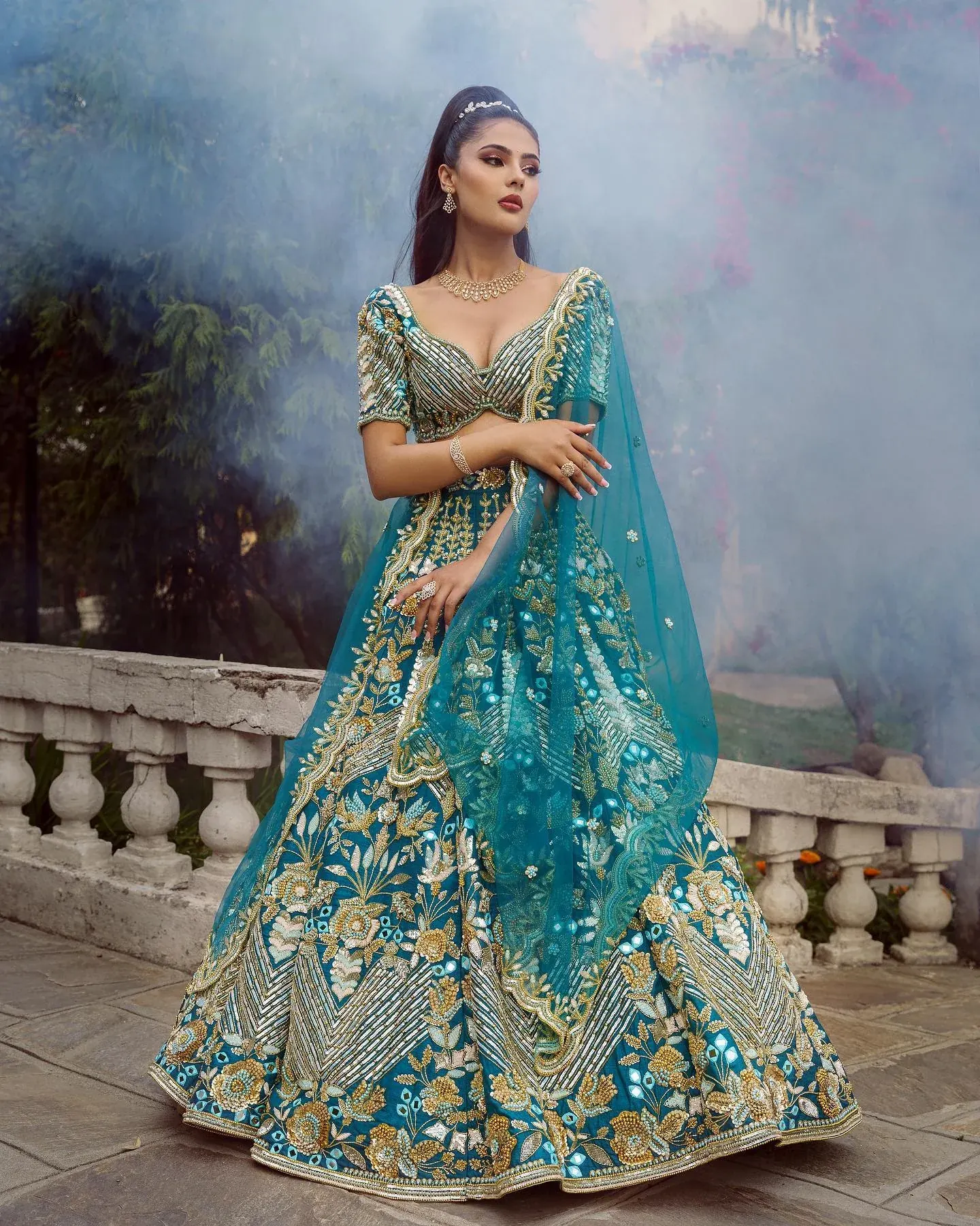 A turquoise lehenga with gold embroidery and a sheer dupatta, photographed in mist.