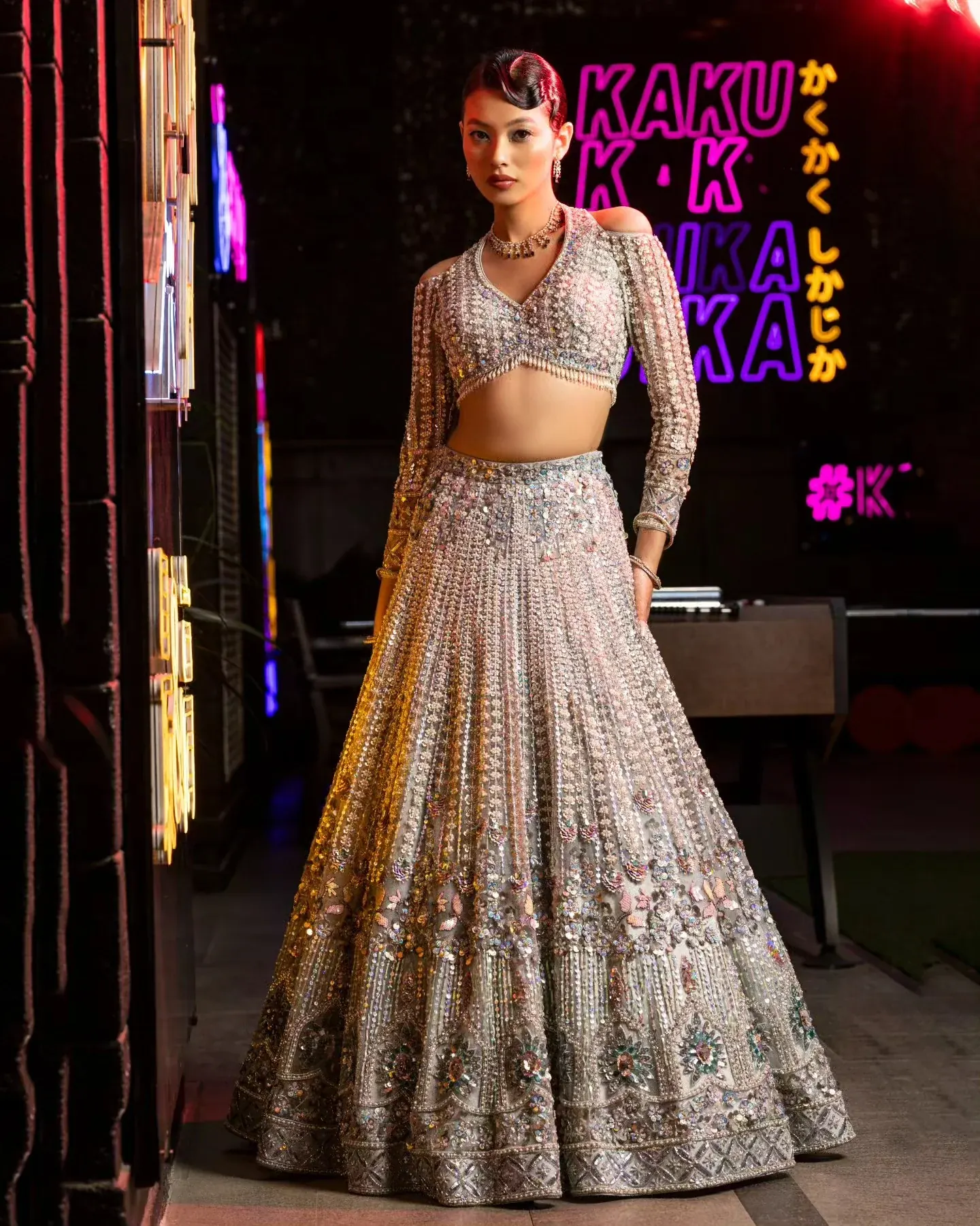 A silver lehenga with a full mirror-worked skirt, photographed against neon light.