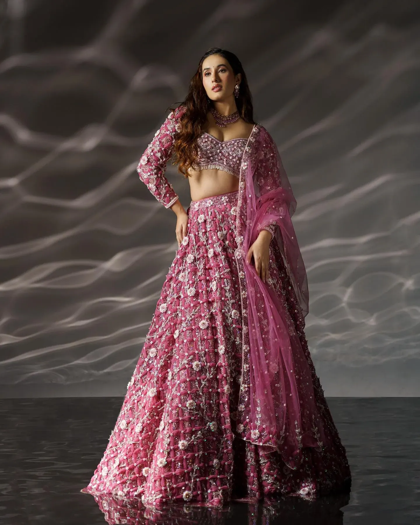 A rose lehenga with floral embroidery and a sheer dupatta, against a grey ground.