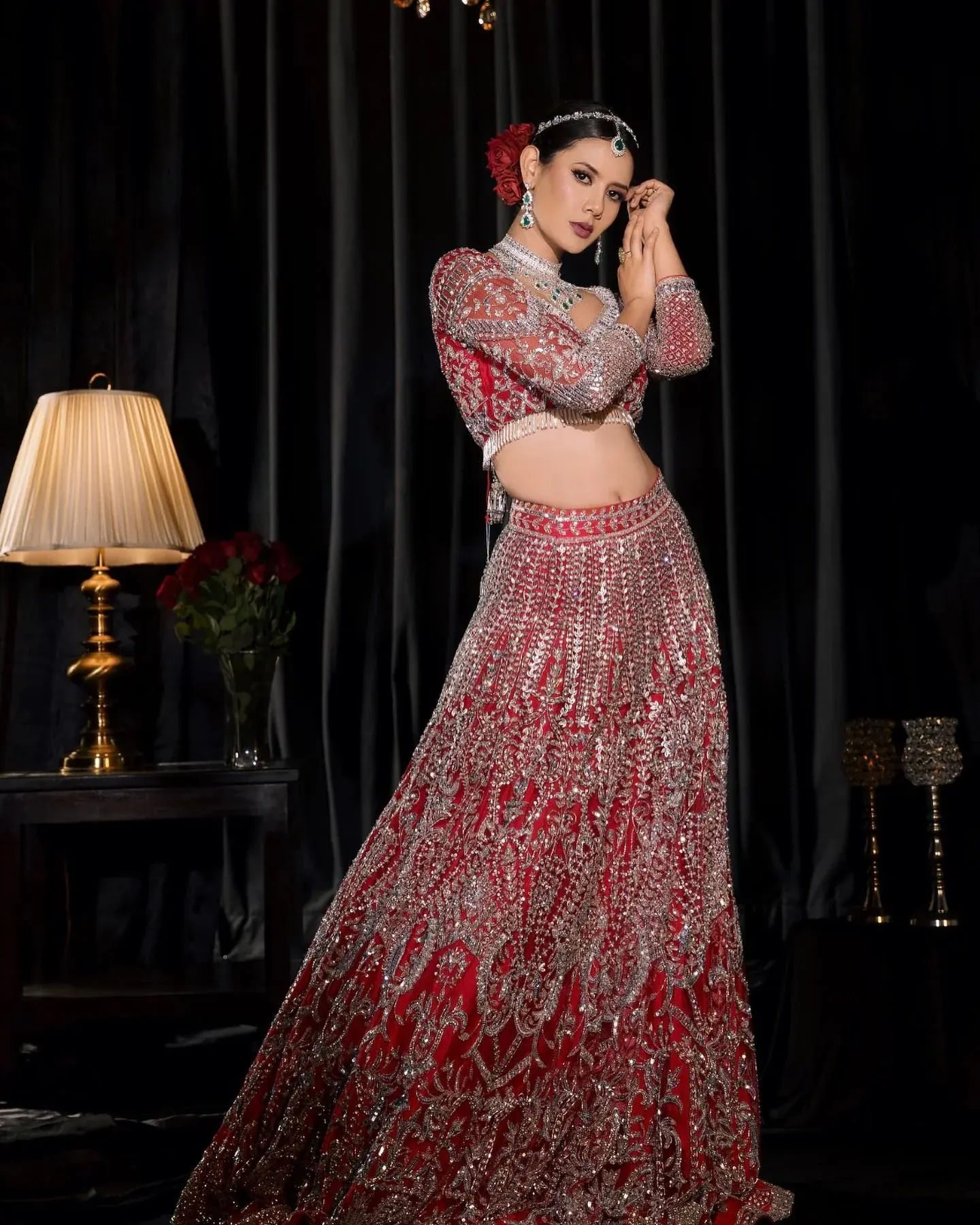 A red ombre lehenga with dense bead work, photographed in a lamplit interior.
