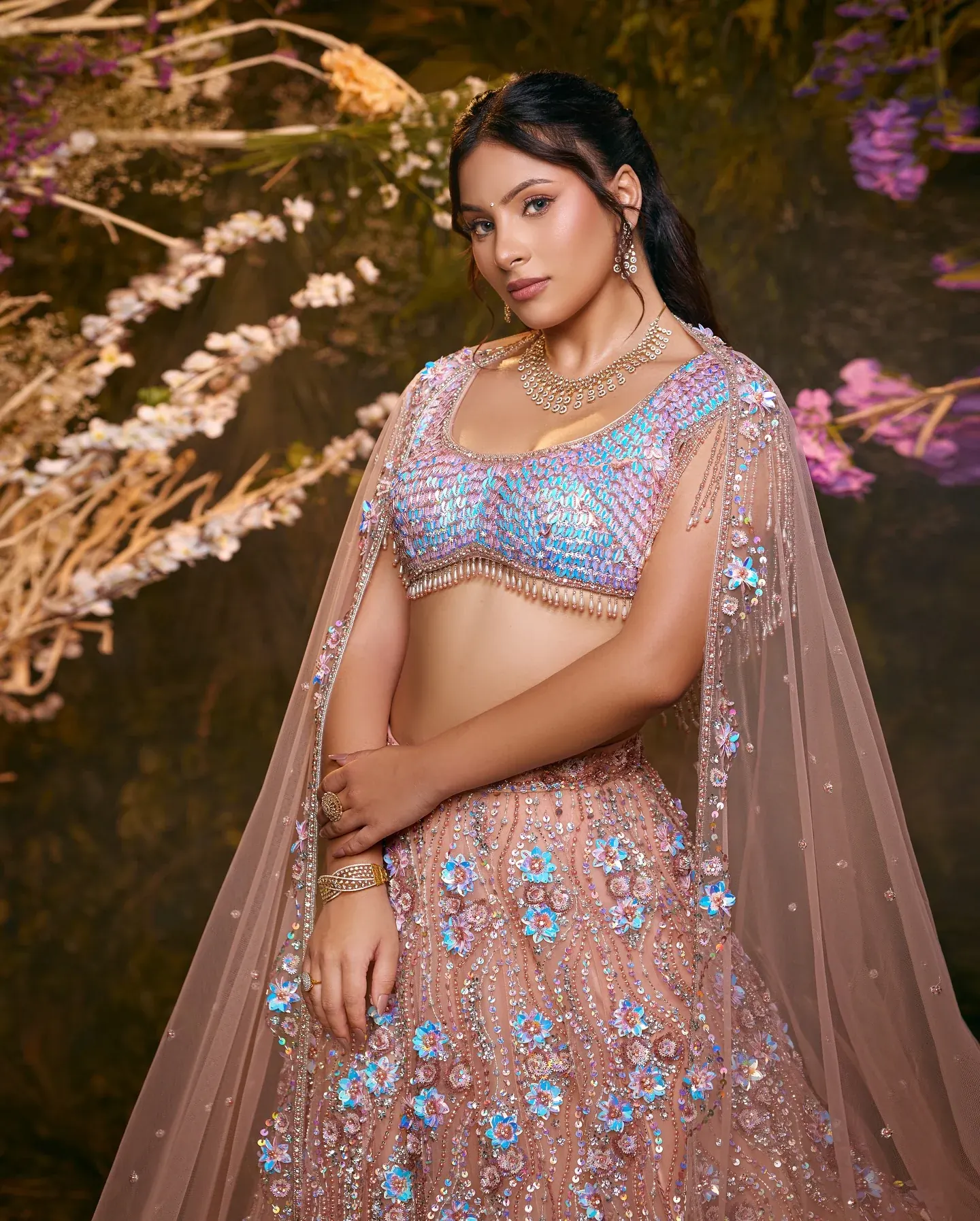 A blush lehenga with blue embroidery and a sheer dupatta, photographed among blossom.