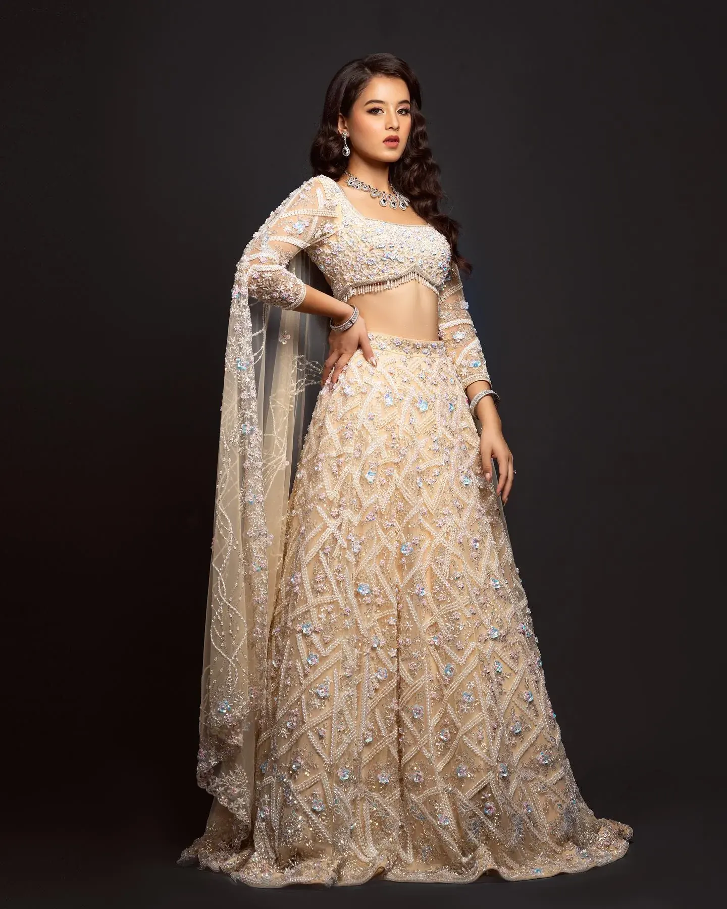 An ivory lehenga with gold thread work and a long dupatta, against a dark ground.