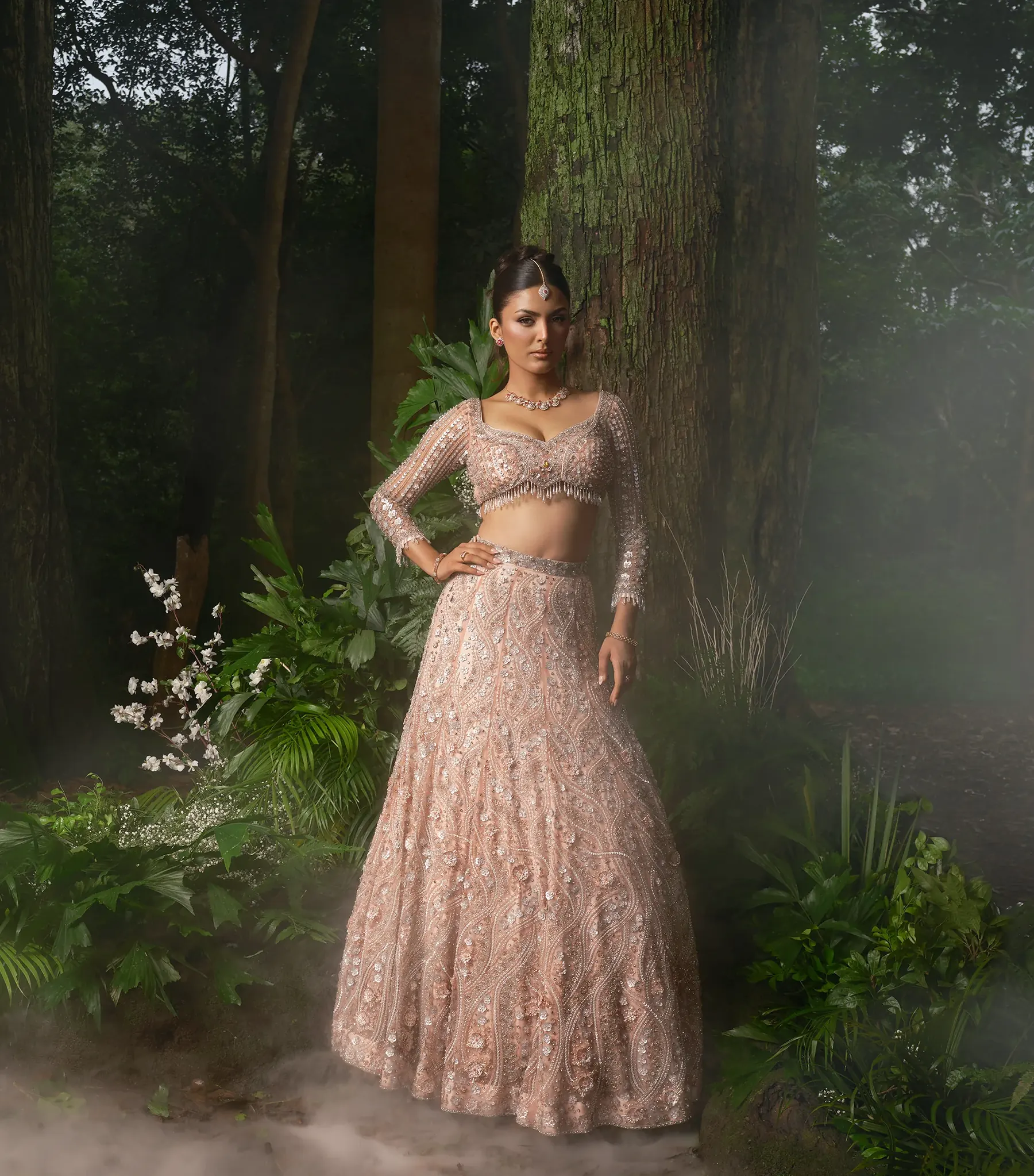 A peach lehenga with a beaded, long-sleeved blouse and a tasselled hem, photographed against a mossy tree in low mist.