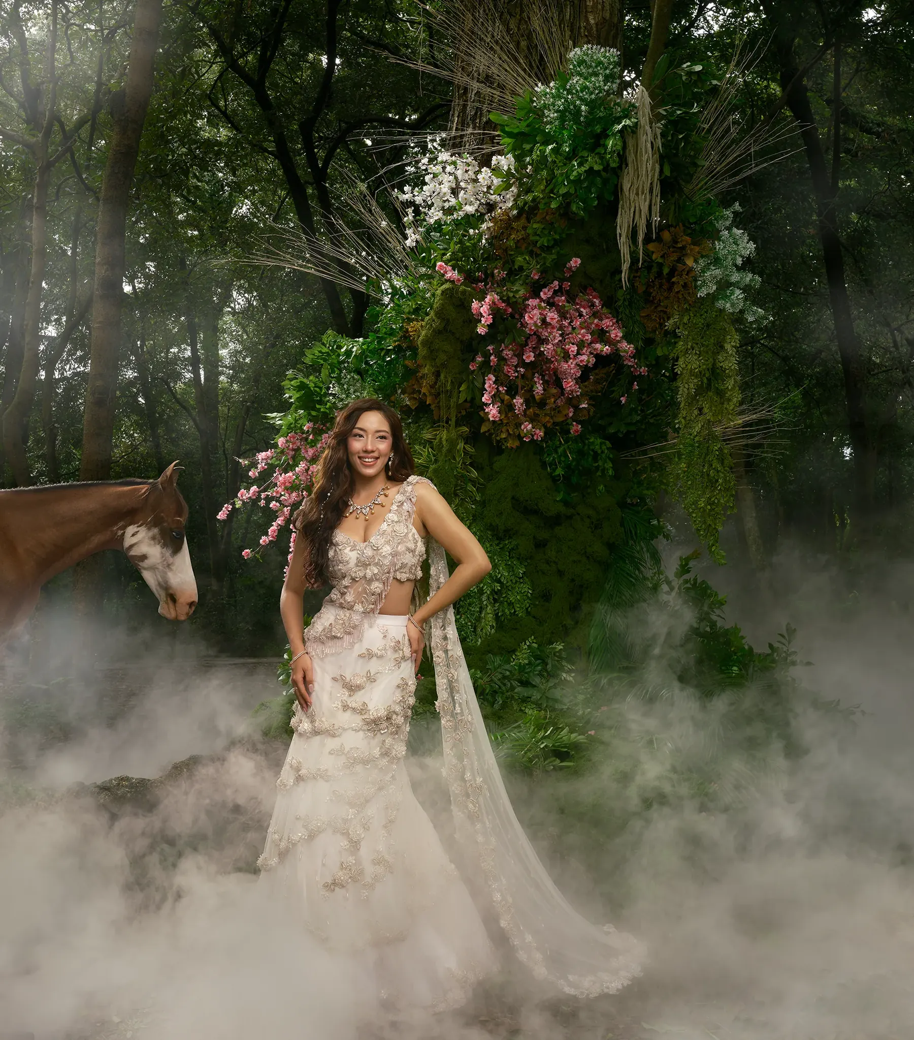 An ivory and champagne fishtail gown with raised floral appliqué and a long embroidered drape, photographed with a horse in dense mist.
